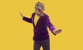 Eccentric funny showman in rubber dinosaur mask and velvet jacket dancing on yellow background.