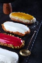 Eclairs in assortment. Multi colored eclairs on dark background. Custard dough.Vertical photo.