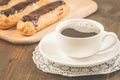Eclairs with chocolate and a coffee cup/eclairs with chocolate and a coffee cup on a wooden background. Selective focus Royalty Free Stock Photo