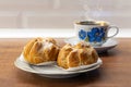 Eclairs with custard and on a white plate. Eclairs with cream filling covered with powdered sugar and cup of black tea with