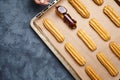 Eclairs, profiterole preparing on baking sheet, spreading chocolate with spoon