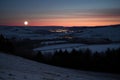 an eclipsed moon over a dark, moonlit landscape