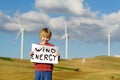 Eco activist boy with banner `Wind Energy` on background of power stations for renewable electric energy production.