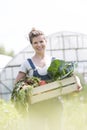 Portrait of smiling mid adult farmer holding vegetable crate at farm