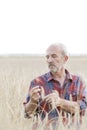 Serious farmer examining wheat crops at farm against sky