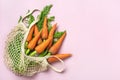 Eco friendly mesh shop bag with fresh harvested carrot isolated on pink background