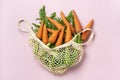 Eco friendly mesh shop bag with fresh harvested carrot isolated on pink background