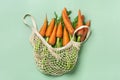 Eco friendly mesh shop bag with fresh harvested carrot isolated on pink background