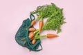 Eco friendly mesh shop bag with fresh harvested carrot on pink background