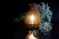 An eco-friendly wooden night light - an interior table lamp shines next to the white flowers of dried flowers on a dark background Royalty Free Stock Photo