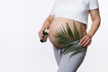 Close-up gravid woman holding palm leaf above her pregnant belly, applying massage oil to reduce prevent stretch marks Royalty Free Stock Photo