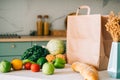 Eco shopping paper bag with fresh vegetables and baguette on the table in modern kitchen. Food delivery or market shopping concept Royalty Free Stock Photo