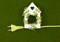Eco wooden house entwined with green leaves and an electric cord on a green grass. Royalty Free Stock Photo