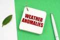 On a white-green surface, a piece of paper, a pen and a notepad with the text - weather anomalies
