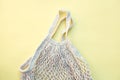 Green and plastic free lifestyle, white eco-friendly string bag isolated on yellow background, responsible consumption