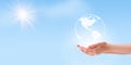 Hand holding white earth globe clouds shape with blue sky and sunlight in background.