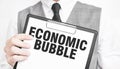 ECONOMIC BUBBLE inscription on a notebook in the hands of a businessman on a gray background, a man points with a finger to the