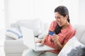 Ecstatic brunette sitting on her sofa using laptop to shop online