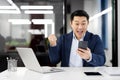 Ecstatic businessman celebrating success with smartphone in modern office Royalty Free Stock Photo