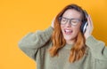 Ecstatic girl with headphones enjoying while listen music isolated on yellow background. Joyful woman with earphones. Happiness