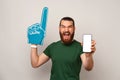 Ecstatic man wearing foam finger fan glove while showing blank phone screen. Royalty Free Stock Photo