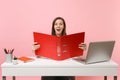 Ecstatic woman looking on red folder with paper documents, working on project while sitting at office with laptop Royalty Free Stock Photo