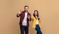 Ecstatic young man and woman dressed in casuals showing OK Okay signs while posing over beige background. Portrait of playful