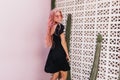 Ecstatic young woman with long wavy pink hair posing with smile beside cactus. Inspired caucasian f