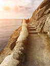 Edge of the cliff with an ancient stone path along the sea with stone steps against the sea with the setting sun, vertical frame Royalty Free Stock Photo