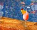 Glass glass with orange cocktail, lemon slice and red cherry at the hotel near the blue water pool. Royalty Free Stock Photo