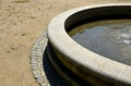 Edge of a stone sandstone circular fountain in the park. built of sandstone filled with water. lined with a light threshing gravel Royalty Free Stock Photo