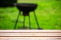 The edge of a wooden table against the backdrop of a blurred barbecue grill and green grass. Place for text