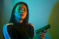 Edgy cinematic portrait of young attractive and dangerous special agent woman or Asian mobster girl holding handgun pointing the