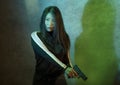 Edgy cinematic portrait of young attractive and dangerous special agent woman or Asian mobster girl holding handgun pointing the