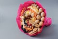 Edible gift bouquet in wrapping red paper made of various dried fruits, nuts, candied fruits for a gift. Gray background, foregrou