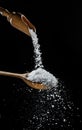 Edible salt crystals falling down into the wooden spoon at black background
