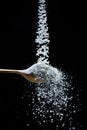 Edible salt crystals falling down into the wooden spoon at black background