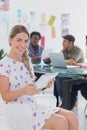 Editor holding tablet and smiling at camera as her team works be Royalty Free Stock Photo