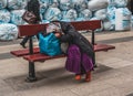 Romanian beggar resting on a bench with her belongings after a hard day of begging