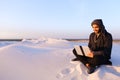 Educated Arab student uses laptop and works sitting on sand amid