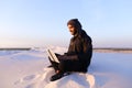 Educated Arab student uses laptop and works sitting on sand amid