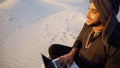 Educated Arab student uses laptop and works sitting on sand amid