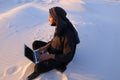 Educated Arab student uses laptop and works sitting on sand amid