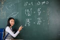 Asian school girl in uniform with backpack on classroom pointing up finger on blackboard Royalty Free Stock Photo