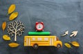 Education and back to school concept. Top view photo of cardboard school bus, alarm clock and pencil next to tree with autumn dry