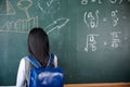 Back view of school girl on science lesson in classroom write an answer on blackboard