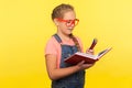 Education and child development. Portrait of creative smart little girl in bright red glasses holding notebook