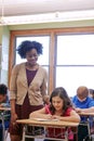 Education, classroom and teacher with girl writing exam or help with test in notebook at Montessori school. Black woman