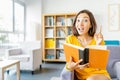 Happy student woman thinking and having interesting idea while reading book in library