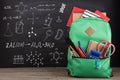 Education concept - school backpack with books and other supplies, blackboard background